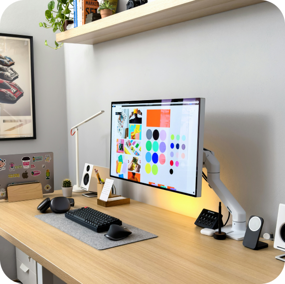 A modern desk with a computer screen displaying color schemes and designs, a keyboard, mouse, and various accessories, including a desk lamp and speakers.